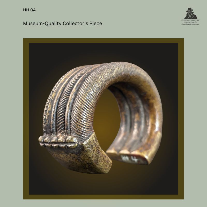 Oblique profile view of a West African brass manilla currency bracelet cast by the lost-wax process, showing finely ribbed decoration, raised border bands and the distinctive flattened terminal. Provenance: Hans Himmelheber Collection, later the Egon Guenther Collection, by family descent to the Thomas Guenther Collection.
