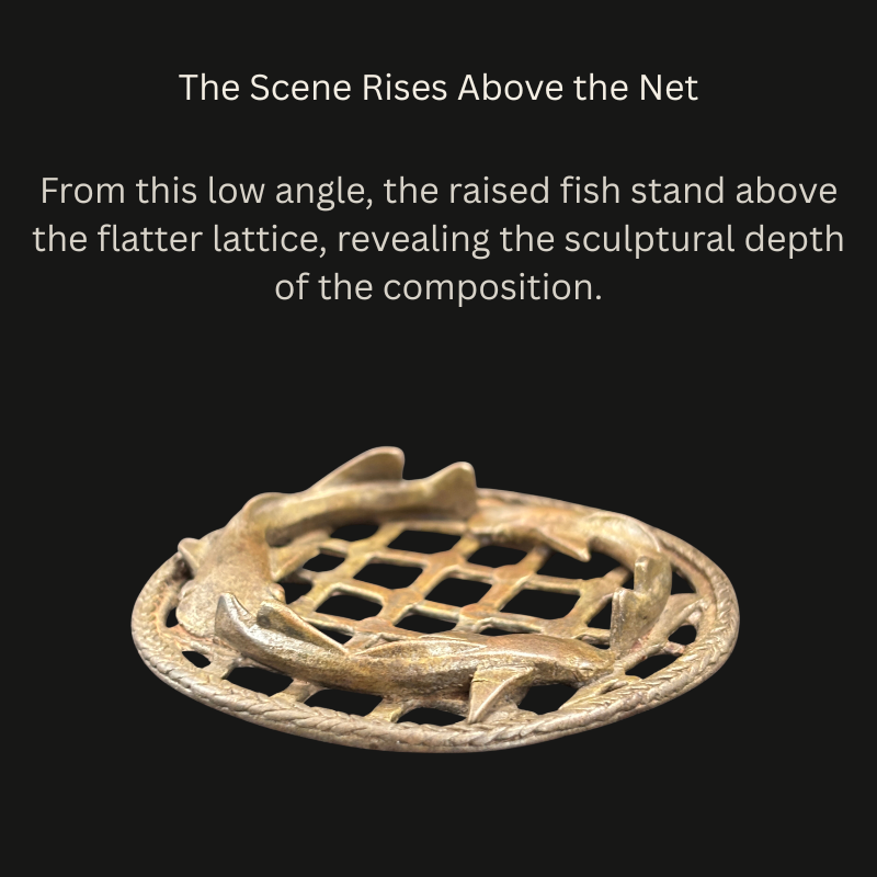 Low-angle view of an Akan cast-brass openwork object, showing raised fish above a net-like lattice enclosed by a twisted-cord border.
