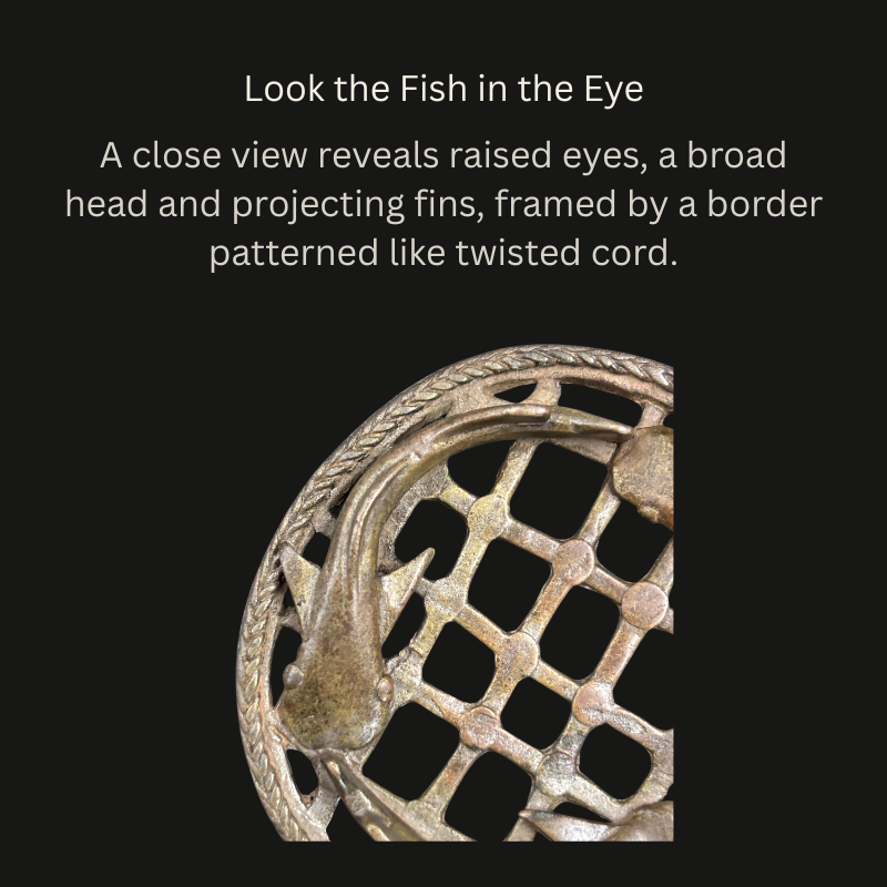 Close-up of an Akan brass openwork object showing a fish with raised eyes, broad head and projecting fins over a lattice, beside a twisted-cord-pattern border.
