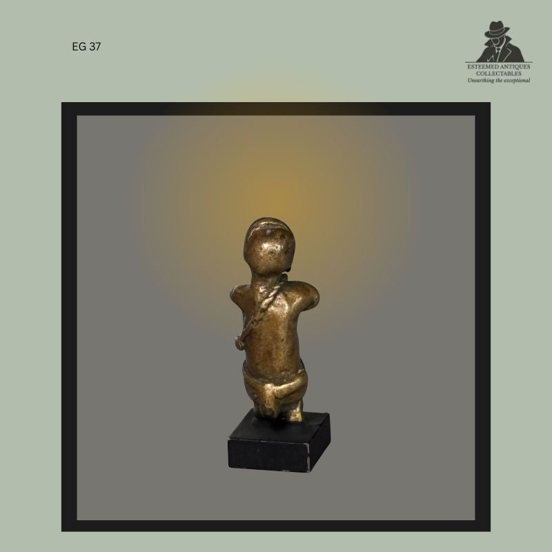 Rear view of an Akan lost-wax cast brass goldweight in the form of a standing human figure, features, rounded torso, and crossed shoulder ornament, Ghana, from the Egon Guenther Collection and later the Thomas Guenther Collection.