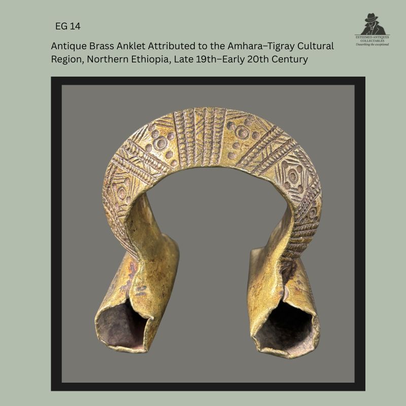 Front view of an antique cast brass anklet attributed to the Amhara–Tigray cultural region of northern Ethiopia, dating from the late 19th to early 20th century, with deeply incised geometric decoration across the arched upper section and flared hollow terminals, from the Egon Guenther Collection.