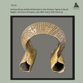 Front view of an antique cast brass anklet attributed to the Amhara–Tigray cultural region of northern Ethiopia, dating from the late 19th to early 20th century, with deeply incised geometric decoration across the arched upper section and flared hollow terminals, from the Egon Guenther Collection.