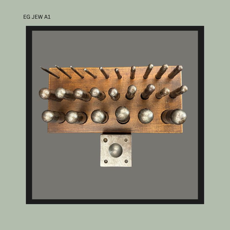 Top view of an antique German jeweller’s doming punch set with graduated steel punches arranged in a fitted wooden stand beside a square steel dapping block, from the Egon Guenther family jewellery tool collection.