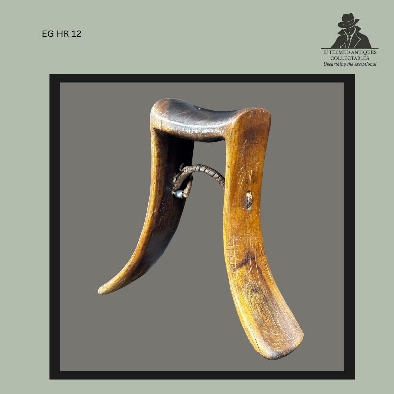 East African carved wooden headrest with flared tapering supports, concave neck rest, and central leather-bound suspension loop, showing surface wear and patina consistent with prolonged use. Provenance: Egon Guenther Collection, by descent to the Thomas Guenther Collection, Netherlands.
