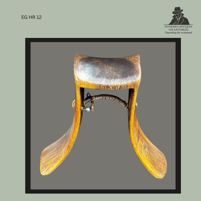 Front view of a traditional East African pastoral headrest carved from wood, featuring a curved sleeping platform supported by flared legs and a leather-bound cross brace, associated with pastoral communities of northern Kenya and northeastern Uganda, from the Egon Guenther Collection.