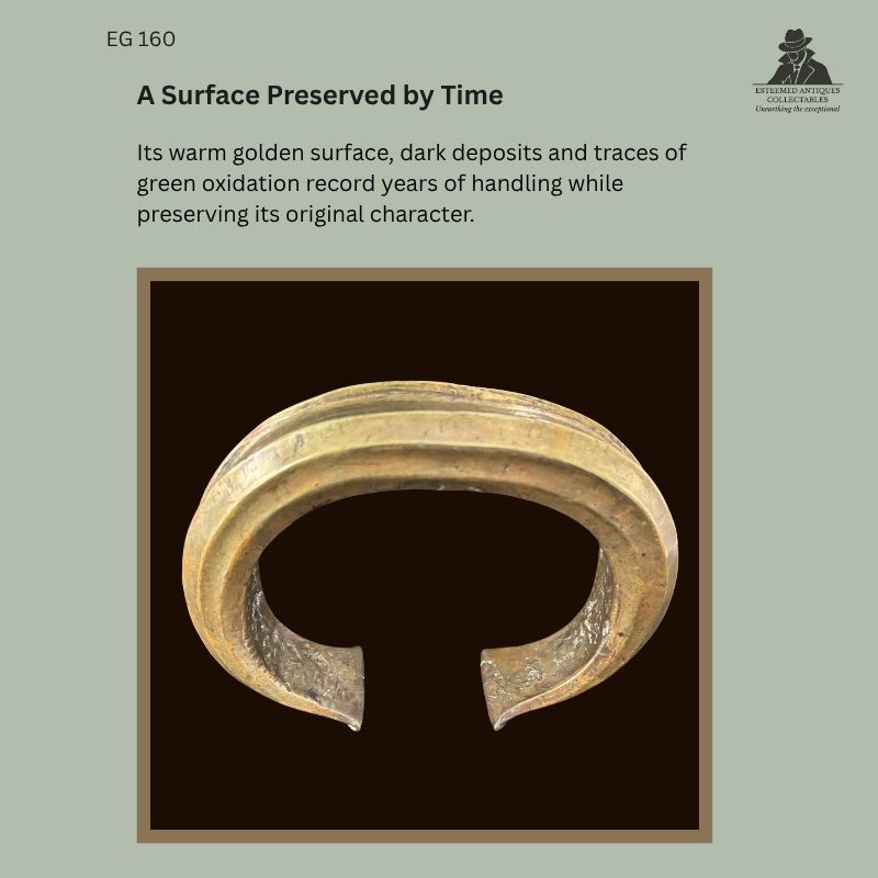 Front view of the massive Fang solid-cast copper-alloy neck torque EG 160 from Gabon, showing its warm golden surface, dark deposits and areas of green oxidation.
