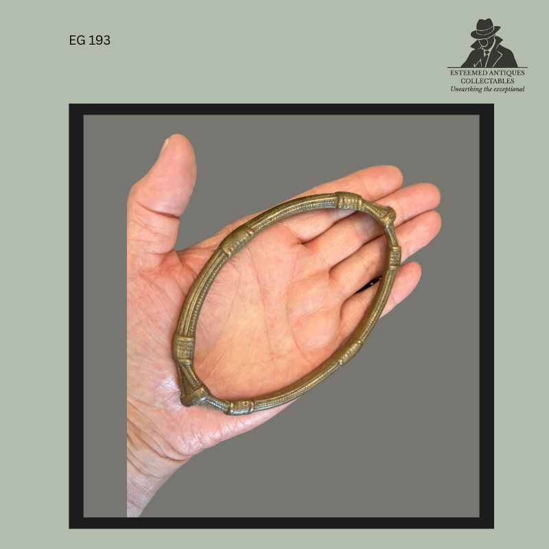 Cast brass or bronze anklet currency attributed to the Frafra or Lobi peoples of West Africa, featuring segmented tubular decoration and hand-worked circular form, photographed in hand for scale, from the Egon Guenther family collection, circa 1900.