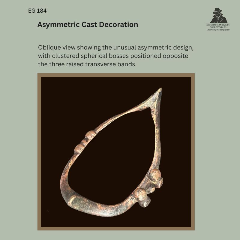 Oblique view of Senufo-attributed boat-form copper-alloy anklet EG 184, showing asymmetric lost-wax cast decoration with clustered spherical bosses opposite three raised transverse bands.