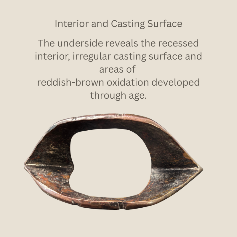 Underside view of the Senufo-attributed copper-alloy boat-form anklet, showing its recessed interior, irregular cast surface and areas of reddish-brown oxidation.