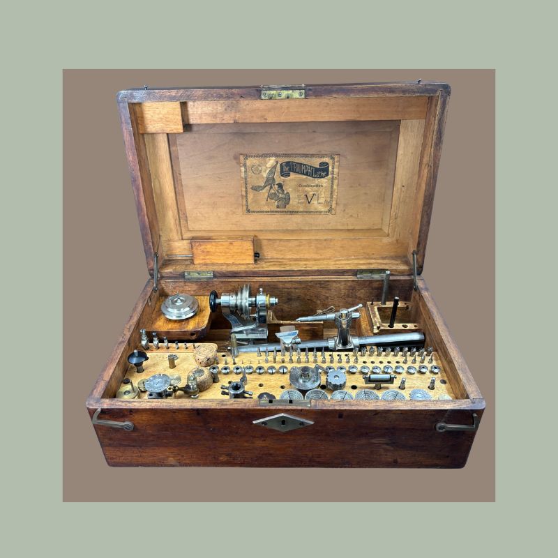 Triumph watchmaker’s lathe and precision horology tool set housed in a fitted wooden case with assorted collets, gears, chucks, and metalworking accessories for fine mechanical and clockmaking work, early 20th century.