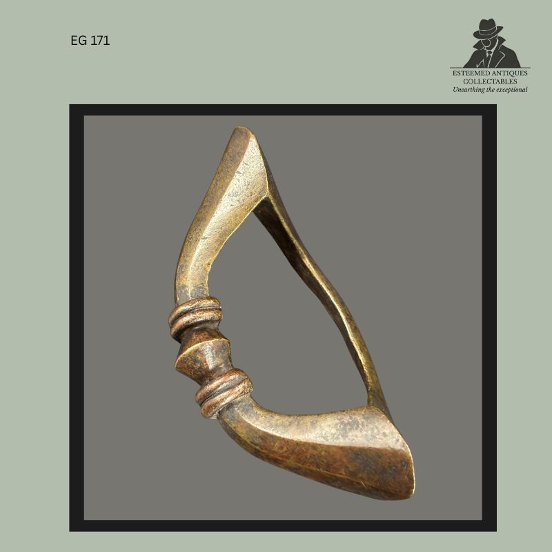 Close view of a West African cast brass anklet currency showing accumulated patina, surface wear, and polished contact areas from prolonged use. The lost-wax cast ornament features a triangular open form with moulded collar decoration and evidence of age consistent with historic personal adornment and prestige currency traditions.