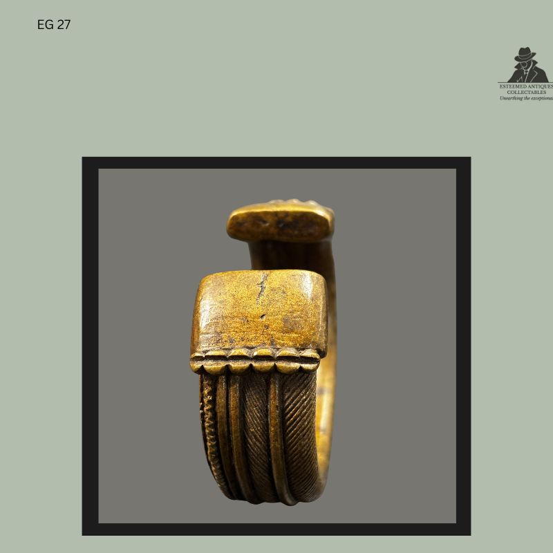 End view of a West African cast brass currency bracelet showing the flattened terminal, raised decorative ridges, and finely textured bands produced using the lost-wax casting technique, from the Egon Guenther family collection.