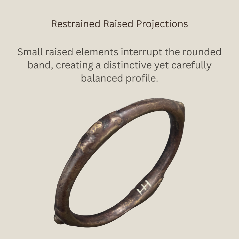 Angled view of a West African copper-alloy bangle showing its rounded band, restrained raised projections, irregular hand-finished surface and dark brown patination.
