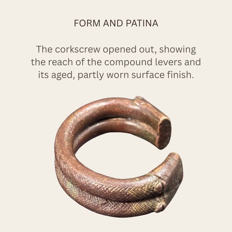 Oblique view of a West African copper-alloy penannular bracelet showing paired decorated ridges, broad flattened terminals, brown patina and patches of green oxidation.