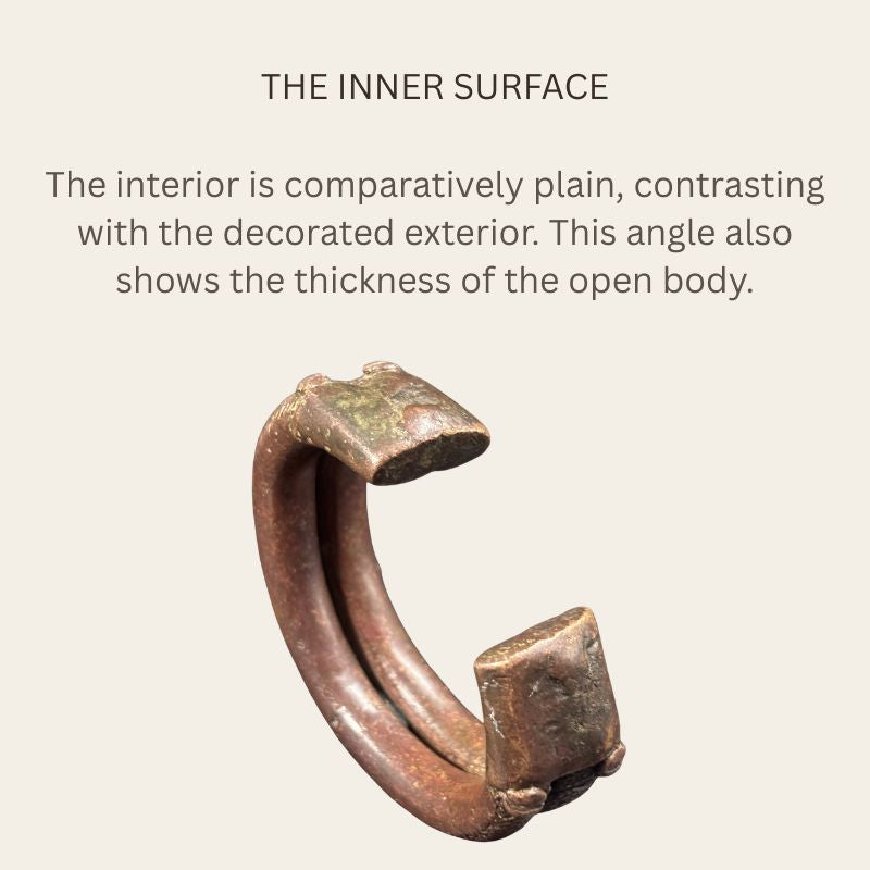 Interior view of a West African copper-alloy penannular bracelet, showing two plain curved inner ridges, broad flattened terminals, brown patina and patches of green oxidation.