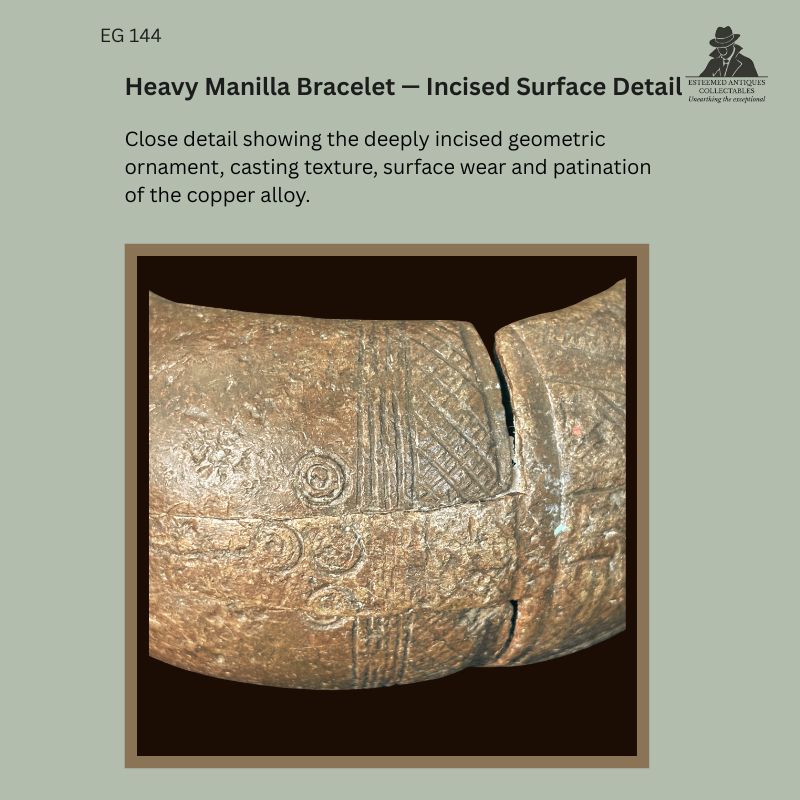 Close-up of West African heavy manilla bracelet EG 144 from Southern Nigeria, showing deeply incised geometric ornament, casting texture, surface wear and patination on the copper-brass alloy.