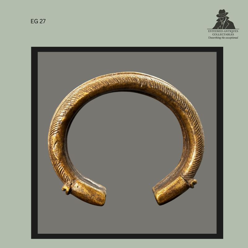 Front view of a West African cast brass bracelet produced using the lost-wax casting technique, showing finely incised decorative surface patterns, open-ended form, and terminal projections, from the Egon Guenther Collection by family descent to the Thomas Guenther Collection.