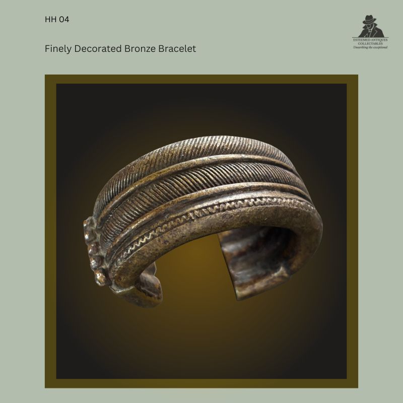 Oblique view of a West African lost-wax cast bronze manilla bracelet showing finely ribbed and incised decorative bands, an open-ended form with expanded terminals, from the Hans Himmelheber Collection, later the Egon Guenther Collection and by family descent to the Thomas Guenther Collection.