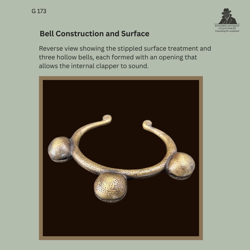 Reverse view of a West African cast brass prestige anklet with three hollow bells, showing stippled surface decoration, open penannular form and rounded terminals from the Egon Guenther Collection.